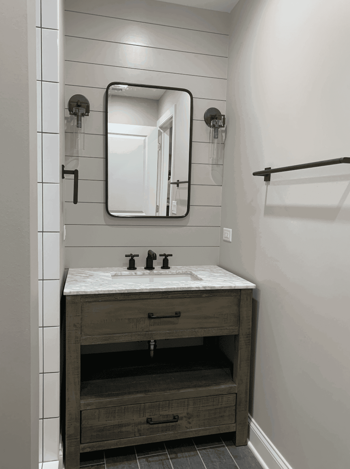 Wood vanity and black-framed mirror against white wall paneling