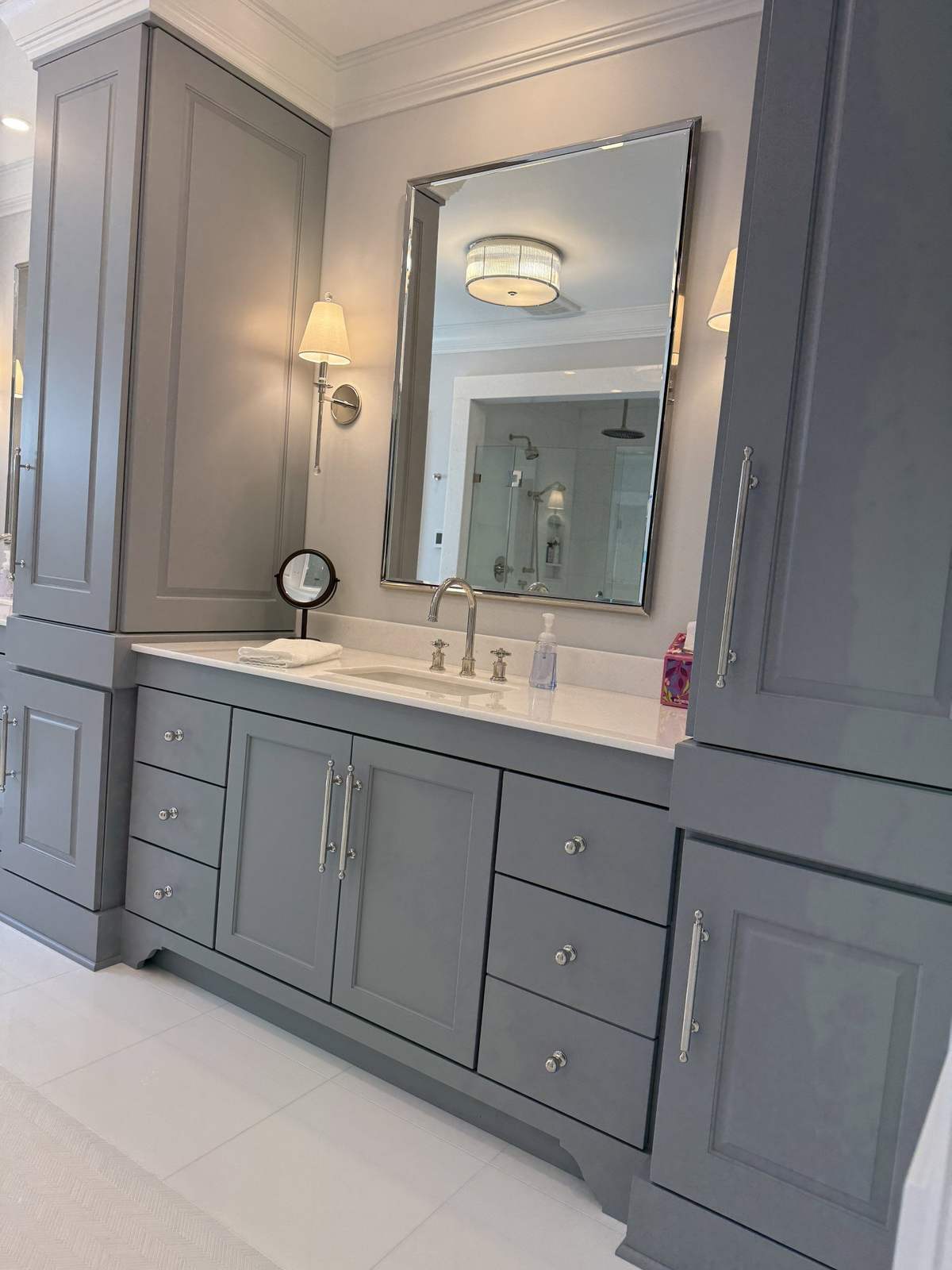 Gray bathroom vanity with tall cabinet and round mirror