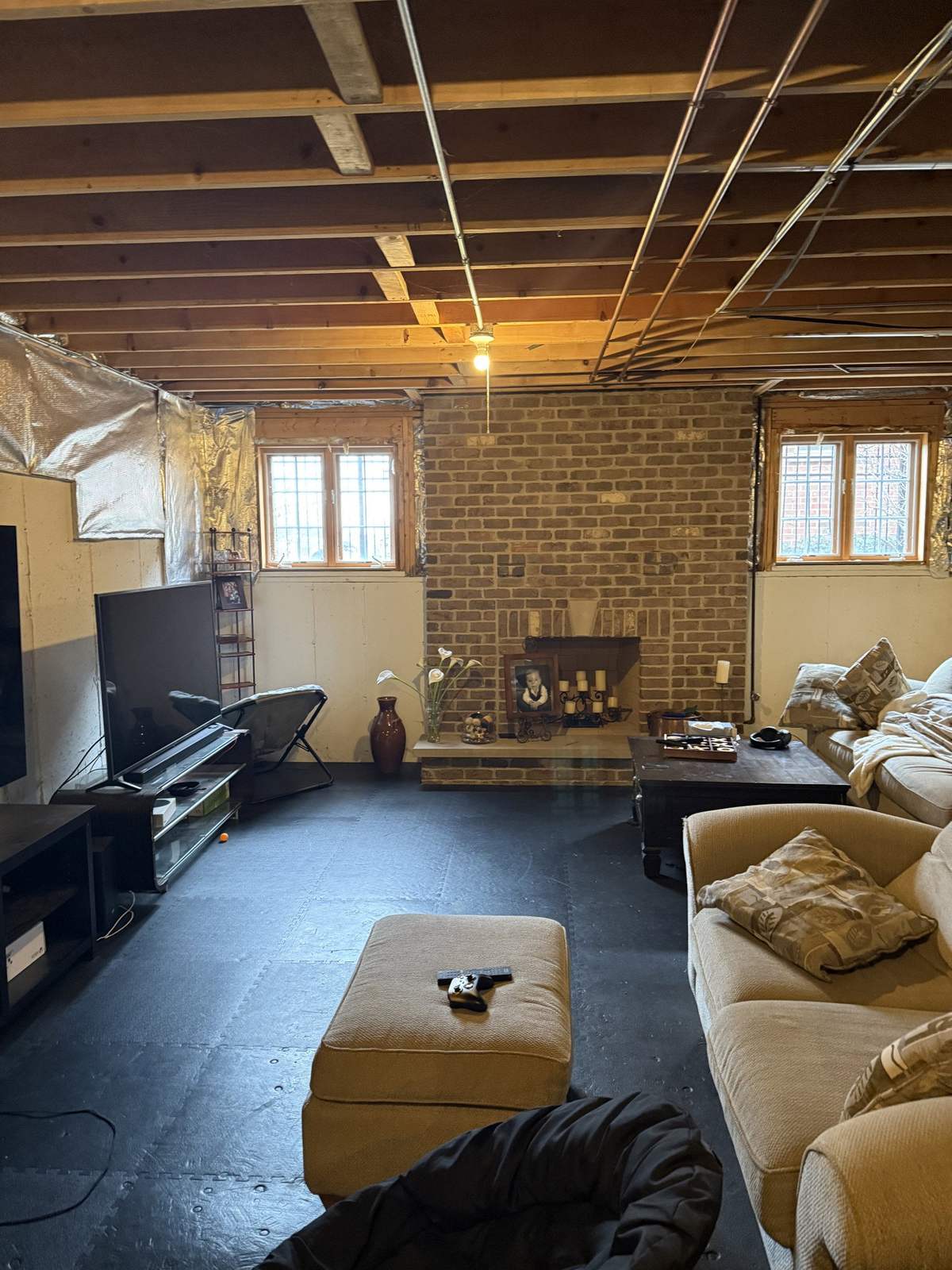 Basement before remodeling with exposed ceiling and brick fireplace