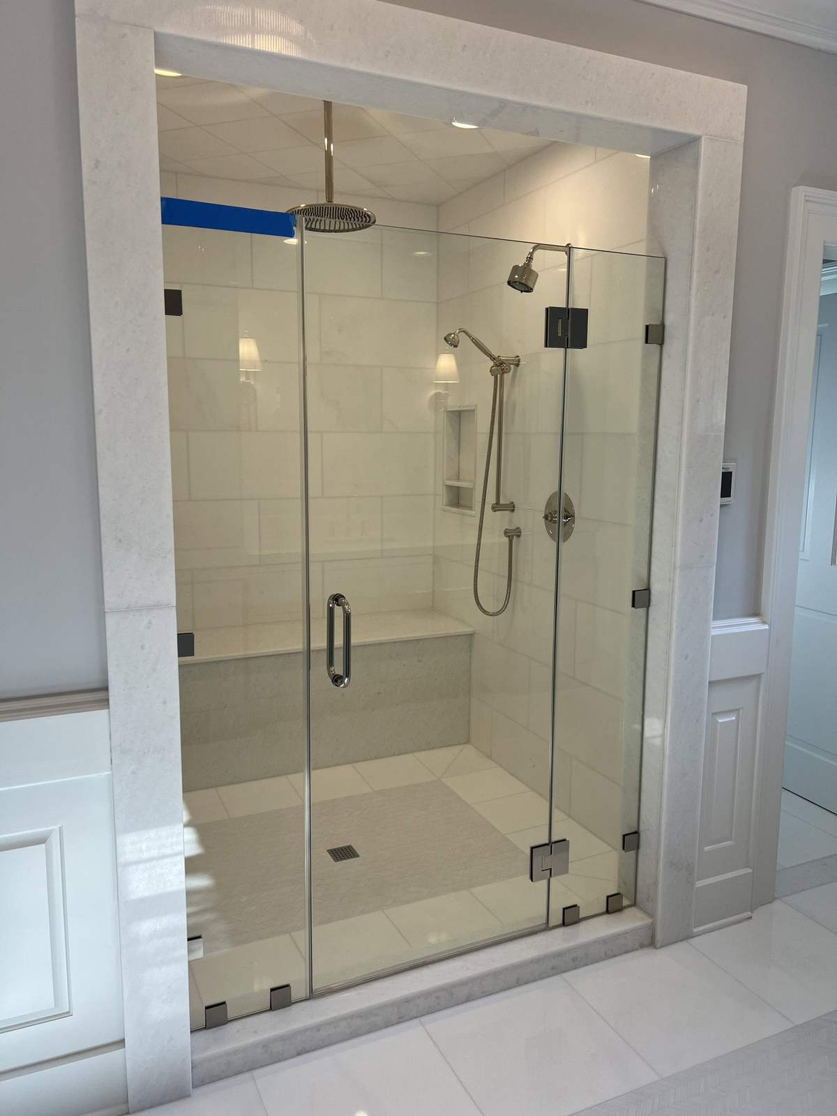 Remodeled shower with light tile and frameless glass door